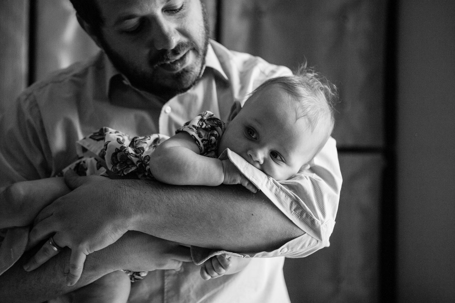 Black and white photo showing a tender moment between parent and sleeping infant held in protective arms.