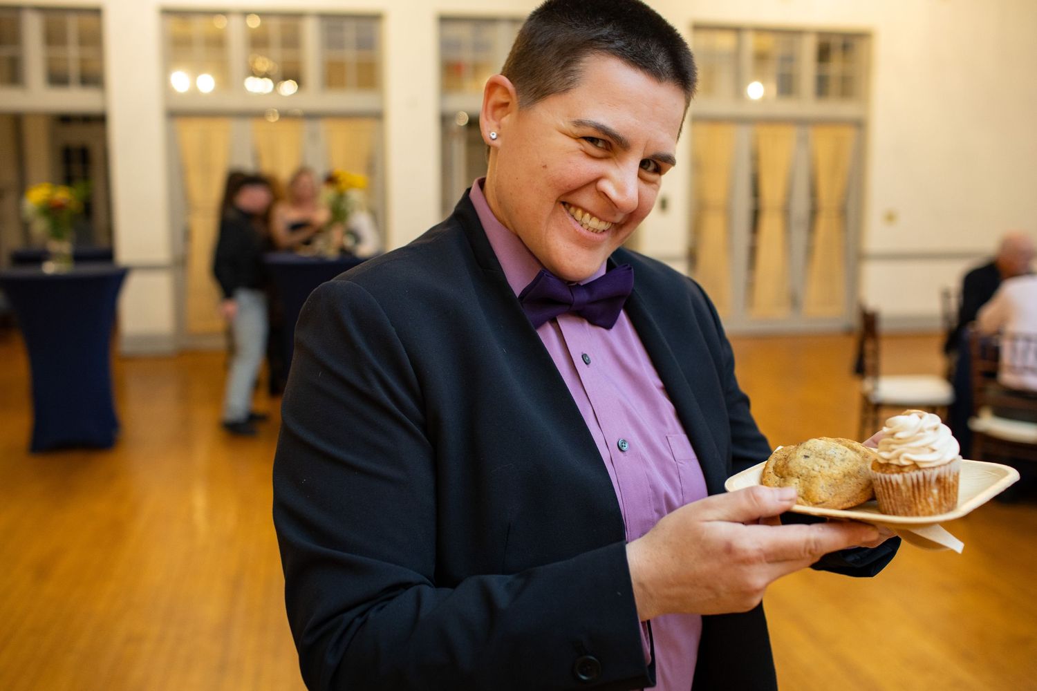 A guest at a formal event enjoying dessert while wearing a black suit and purple bowtie.