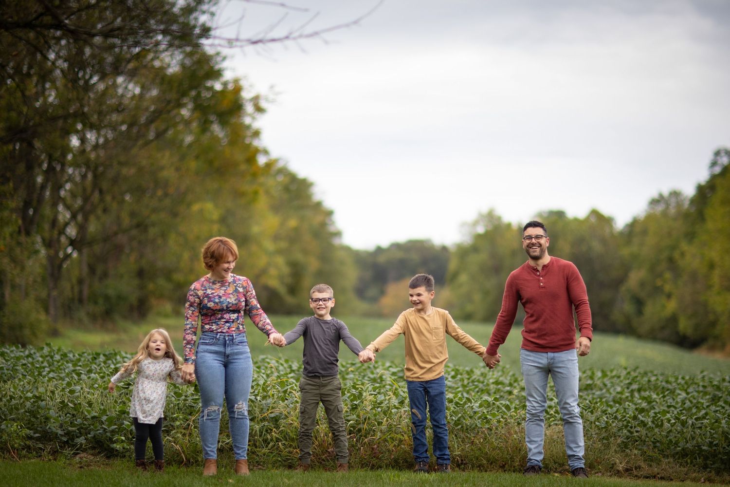 A family holds hands while walking together through a lush green field on an autumn day.