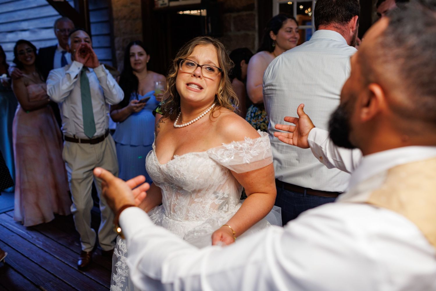 Bride in off-shoulder lace gown dancing joyfully with groom at outdoor wedding reception celebration.