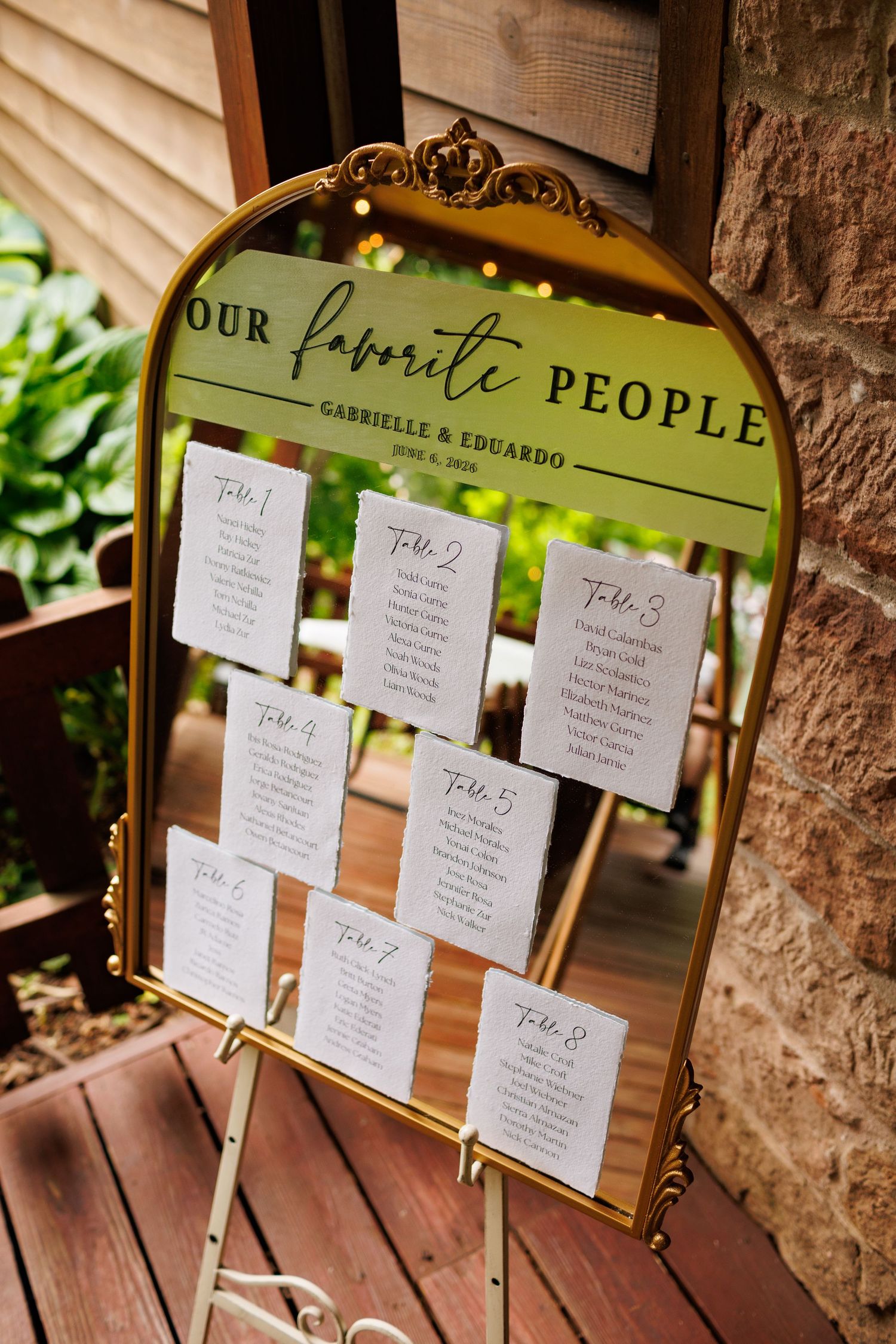 Gold-framed mirror seating chart display reading Our Favorite People for Gabrielle and Eduardo wedding reception.