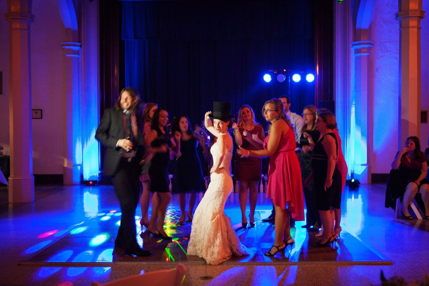 A wedding celebration in progress with blue mood lighting as people dance on a ballroom floor.