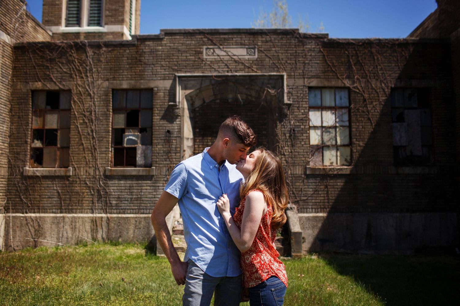 Couple sharing an intimate moment in front of a brick building on a sunny day.