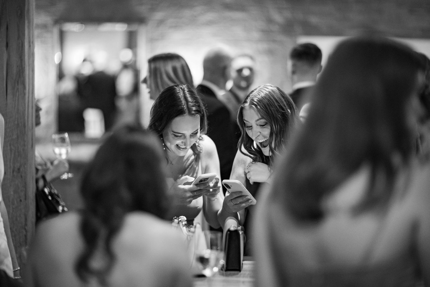 Guests checking phones at wedding reception in black and white candid photo.