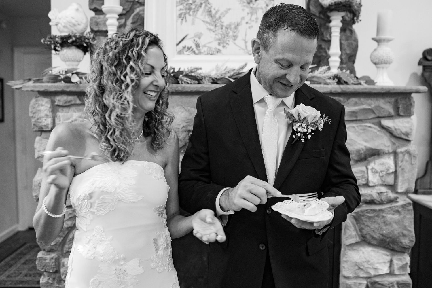 Bride and groom smiling while cutting their wedding cake together in a black and white photo.