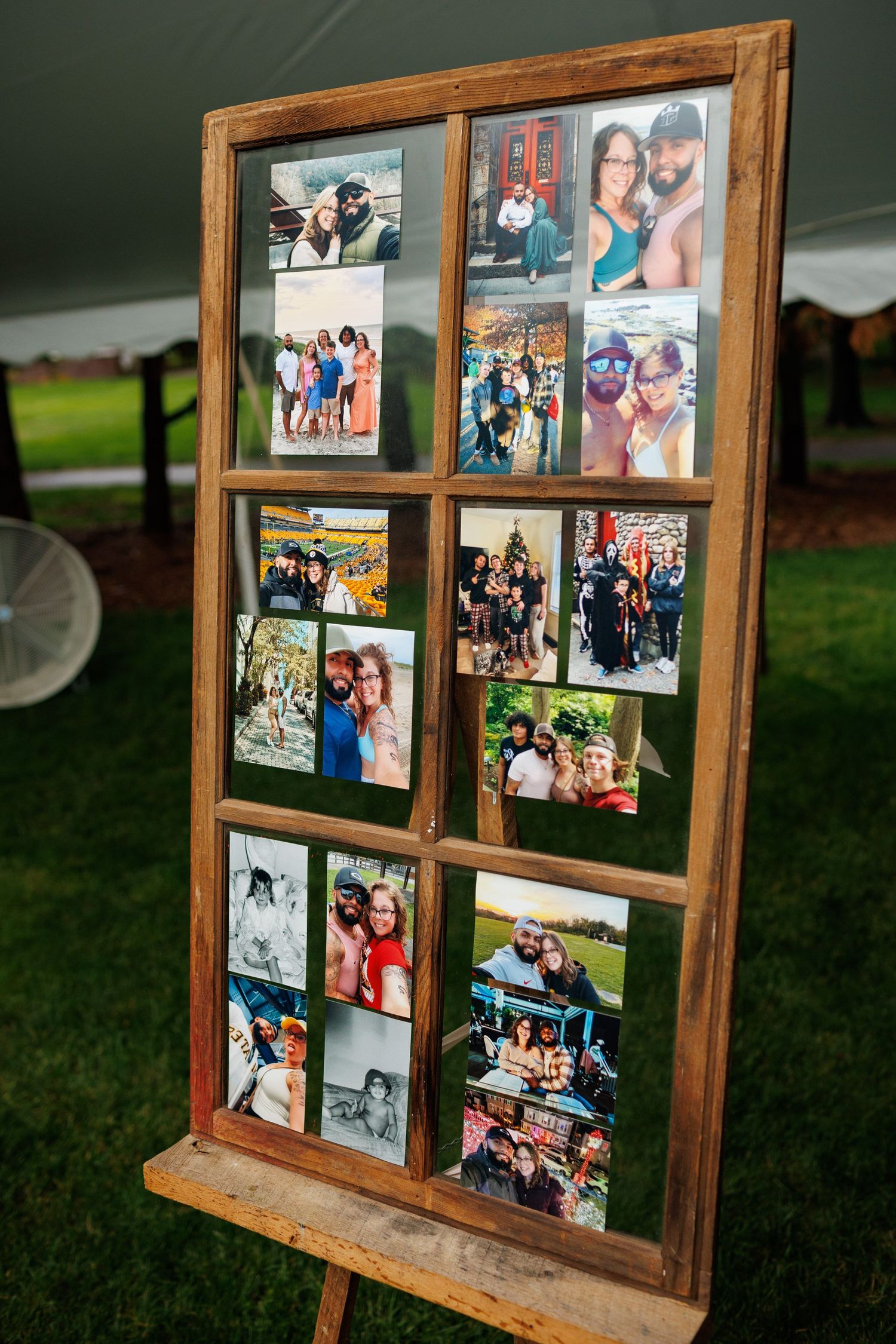 Rustic wooden window frame display with couples and friends photos on an easel at outdoor wedding reception.