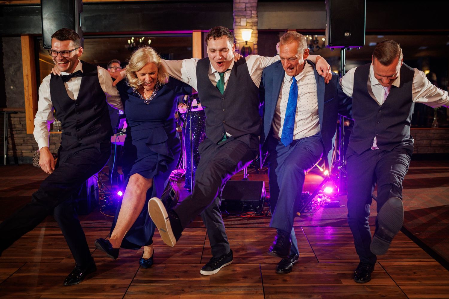 Group of five wedding guests dance energetically together on reception dance floor.