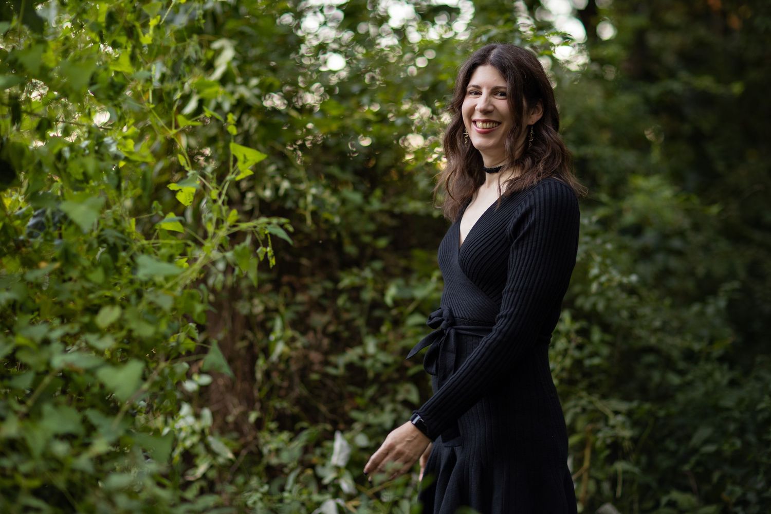 A woman in a black cardigan walking through a lush green garden setting.