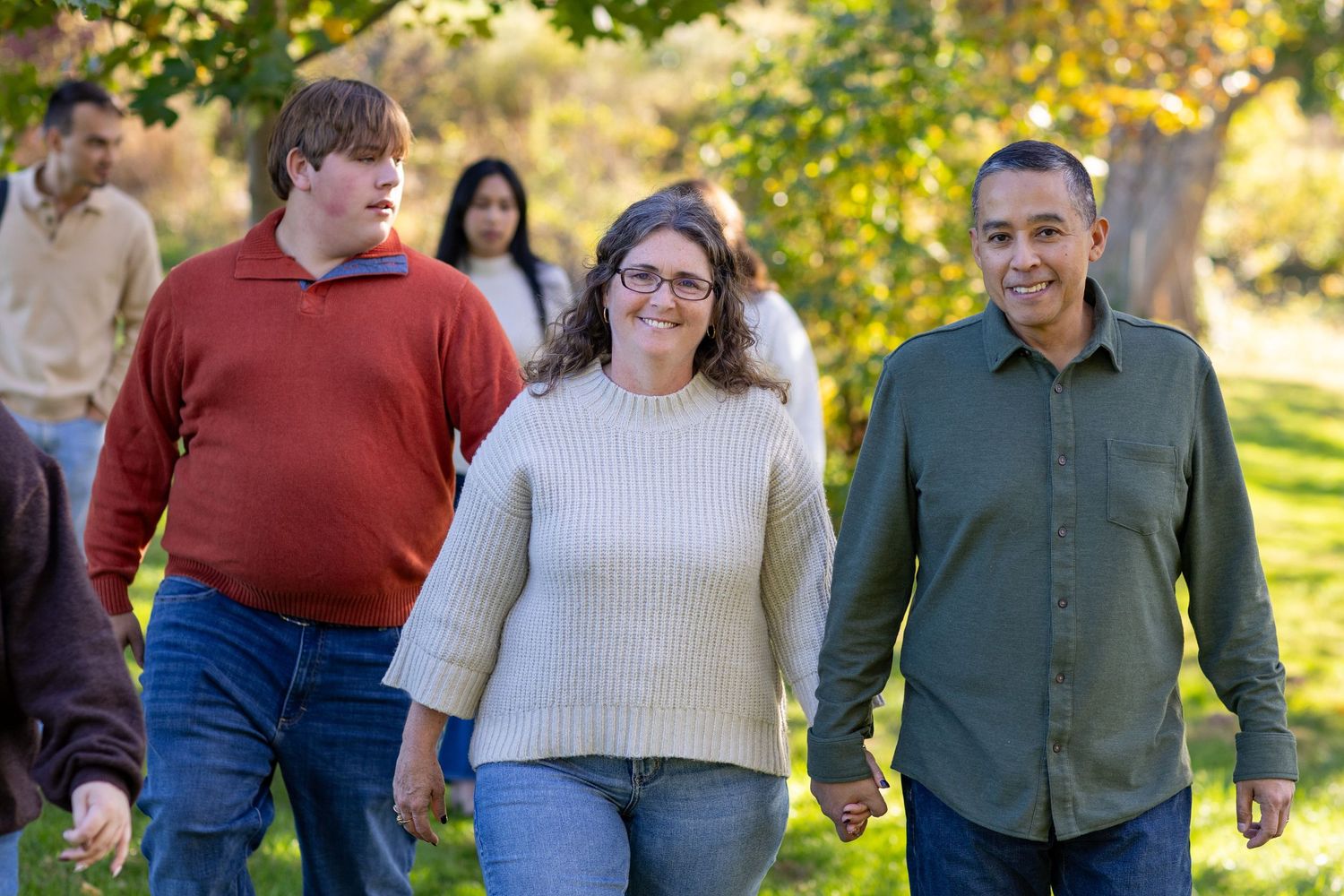 A group of people walking together outdoors on a sunny autumn day with golden foliage in the background.