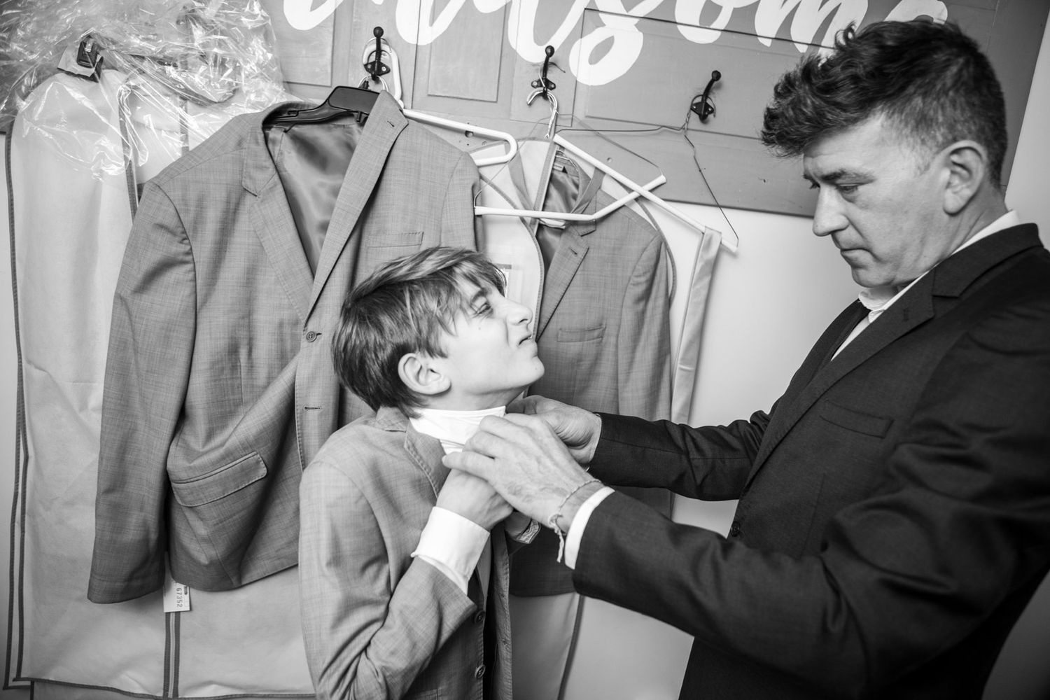 the groom's son does not want to get his tie on, his dad helps, this is a documentary, photojournalistic moment captured in a real situation