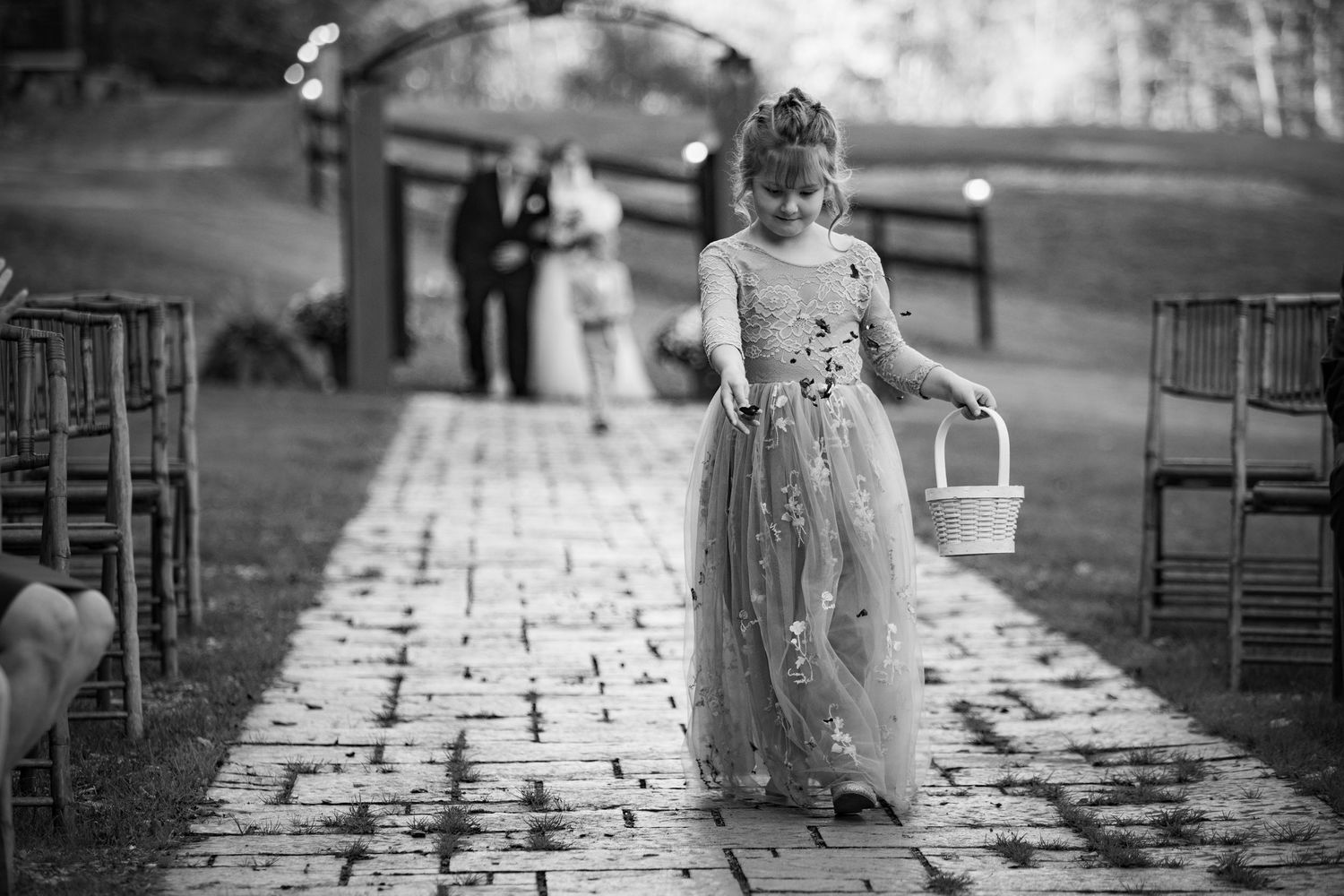 A flower girl in a floral gown walks down the aisle at an outdoor wedding ceremony.