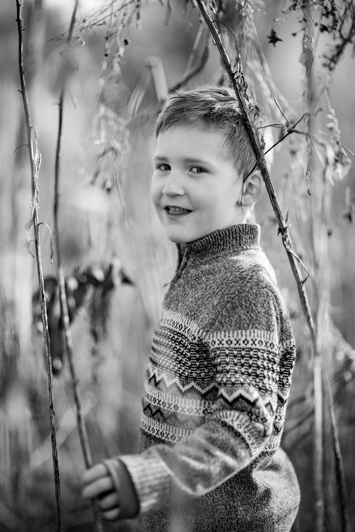 Black and white portrait series showing a child in a patterned knit sweater among tree branches.