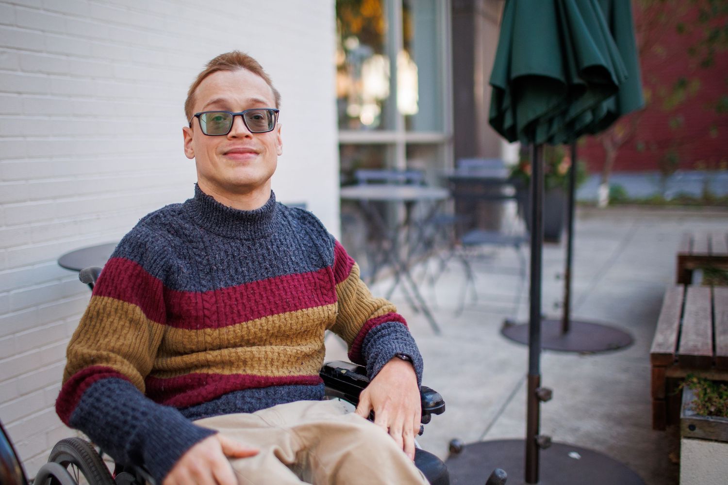 A person wearing a patterned sweater sits casually in a chair while smiling at the camera.