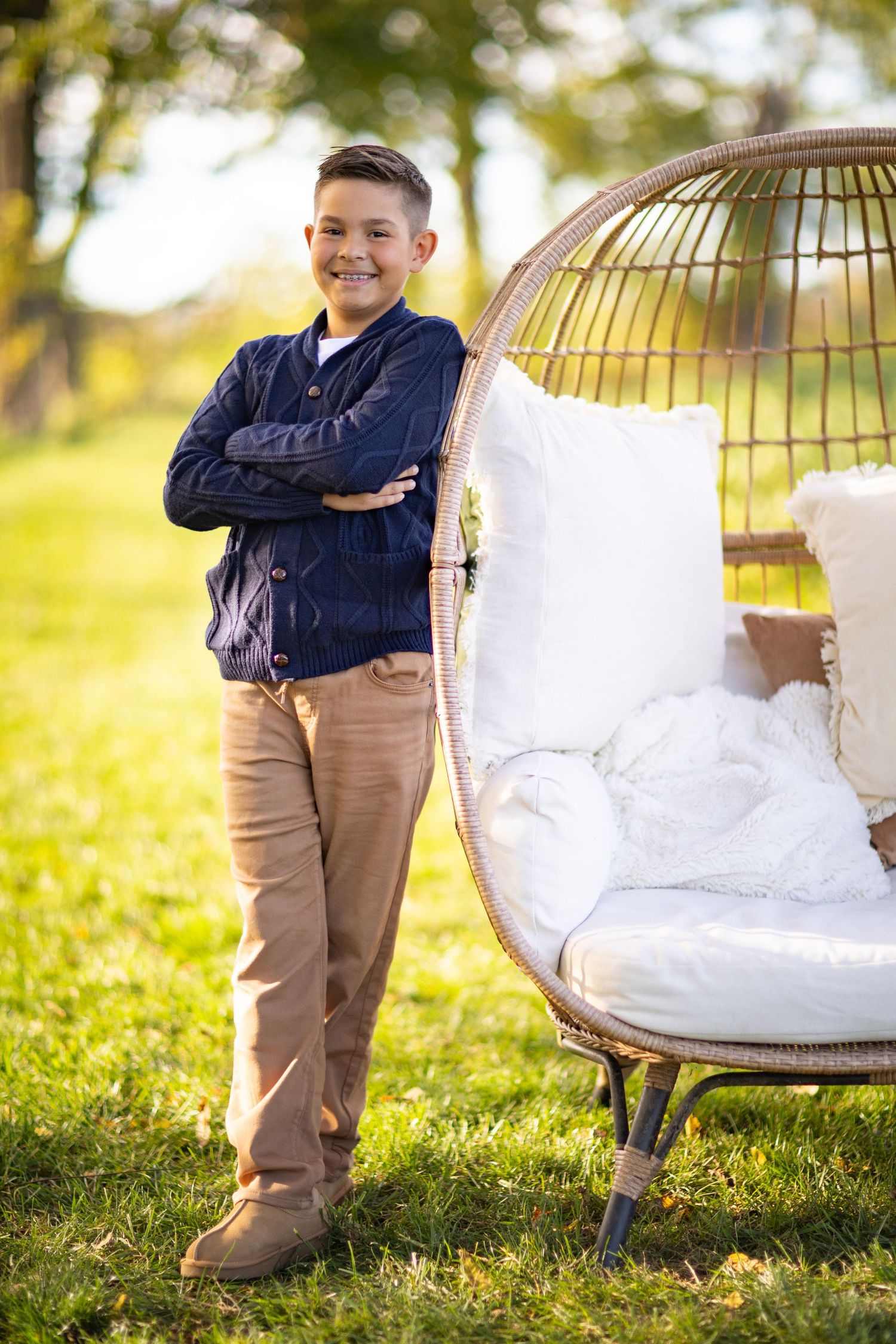 A young child in navy blue shirt and khaki pants stands outdoors near a decorative white chair on grassy ground.