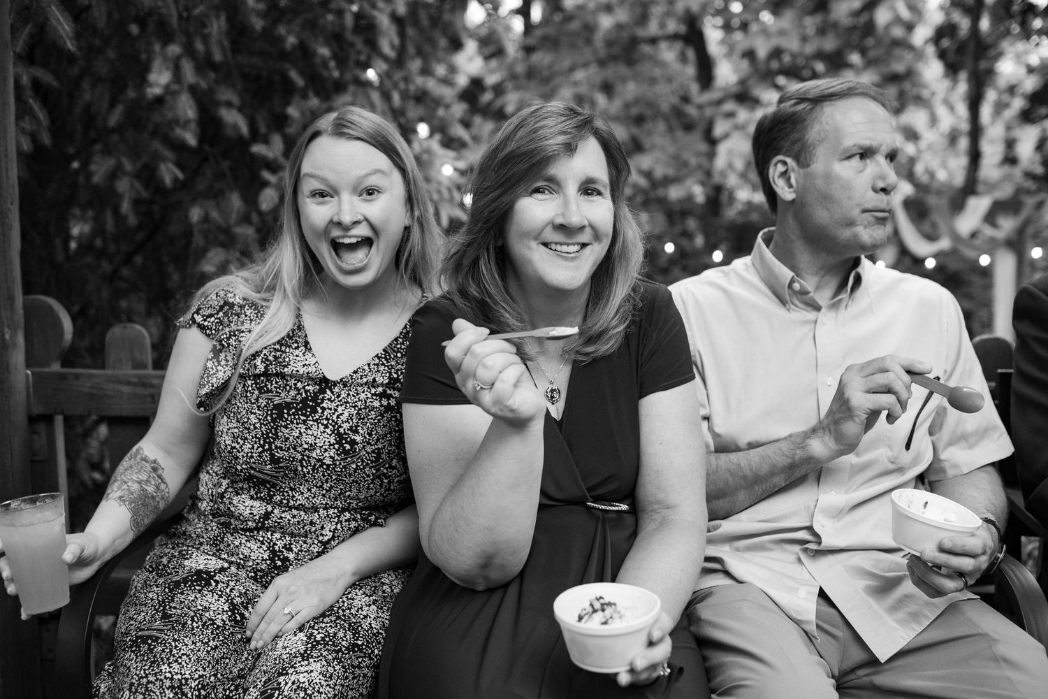 Black and white photo of three wedding guests laughing and enjoying ice cream at reception.