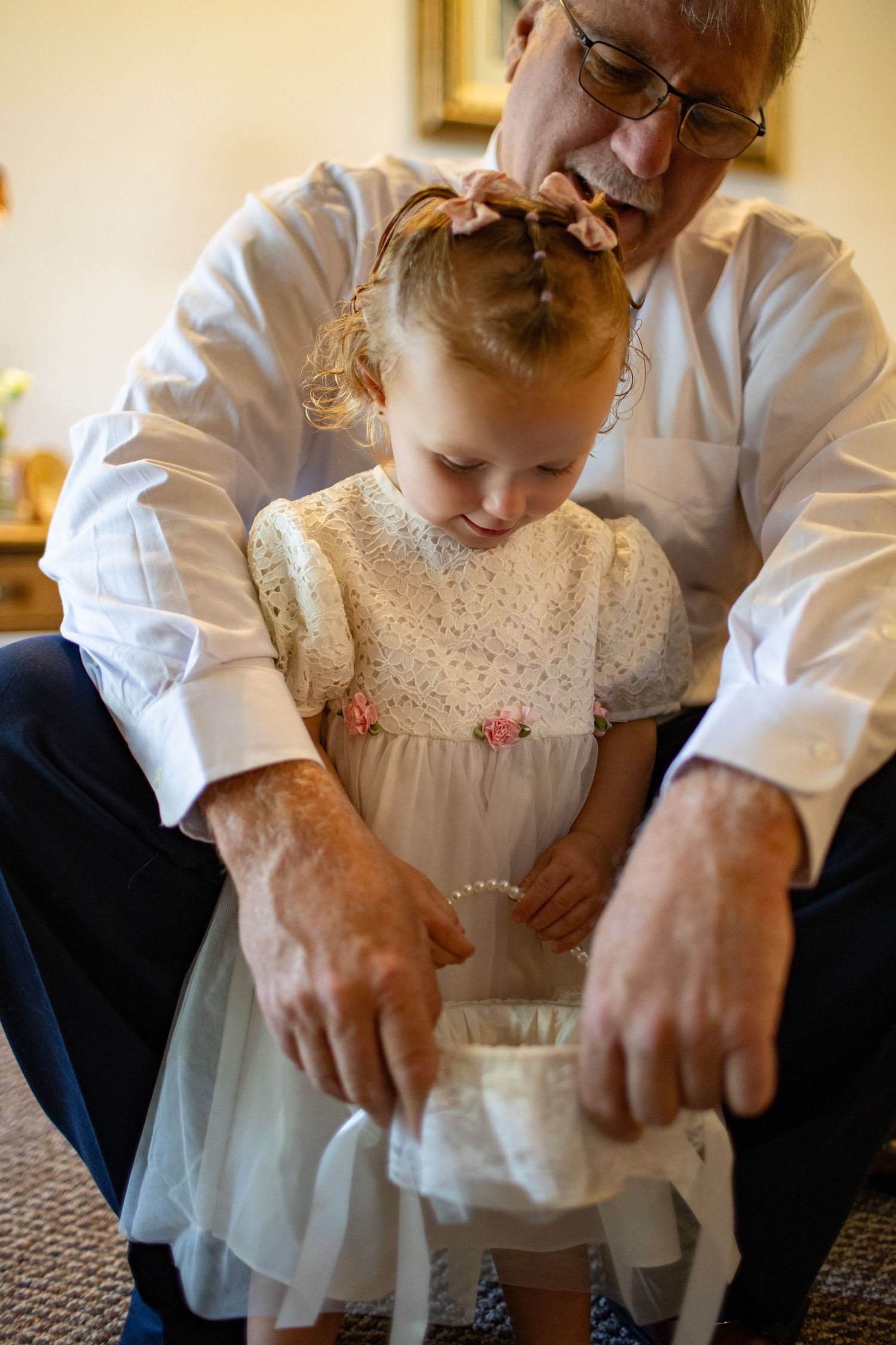 Hands adjusting a white ceremonial dress and beaded necklace in an intimate wedding preparation moment.