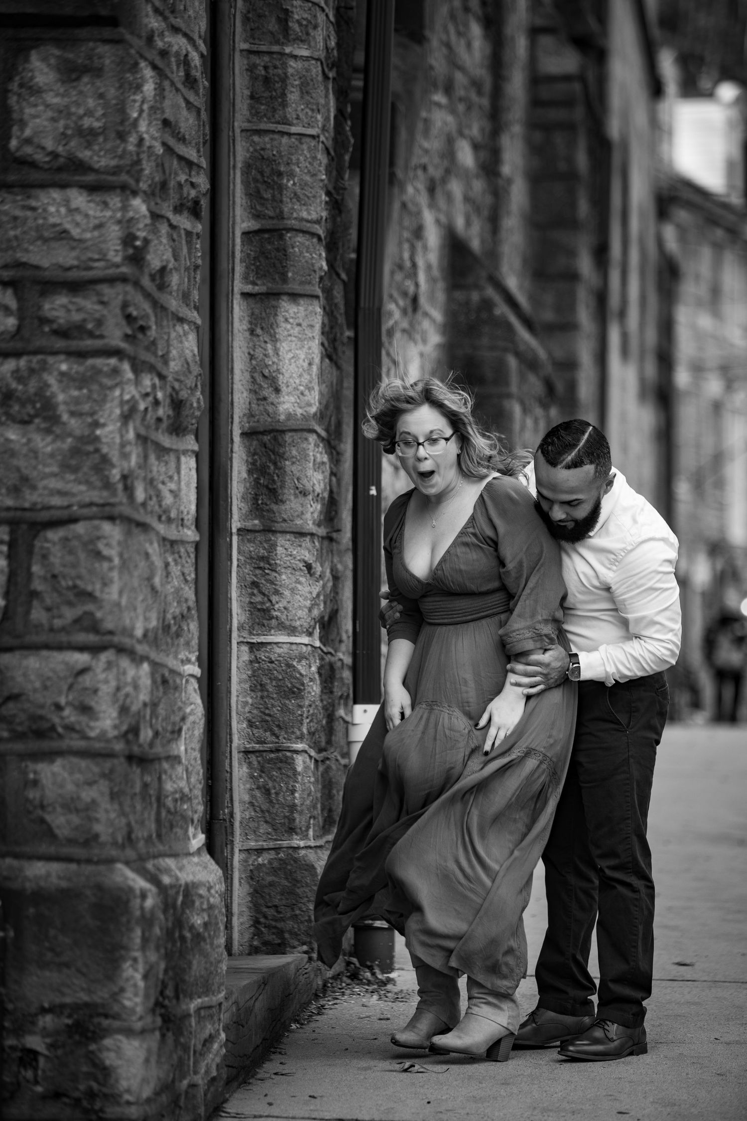 A black and white photo sequence shows two people in casual attire interacting near a stone wall on a city street.