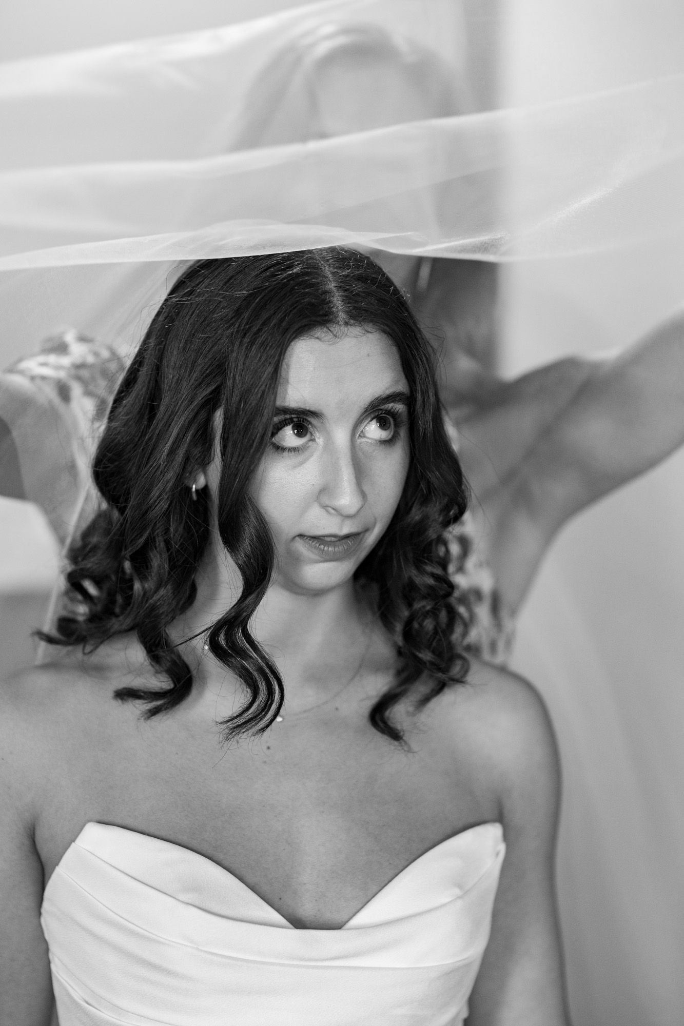 Black and white portrait of brunette bride under veil in strapless gown with soft curled hair.