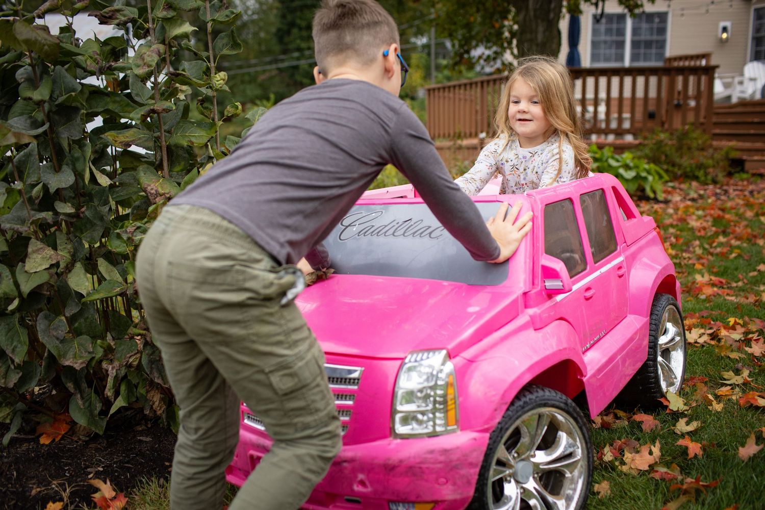 A bright pink toy car being examined outdoors on a fall day with leaves scattered around.
