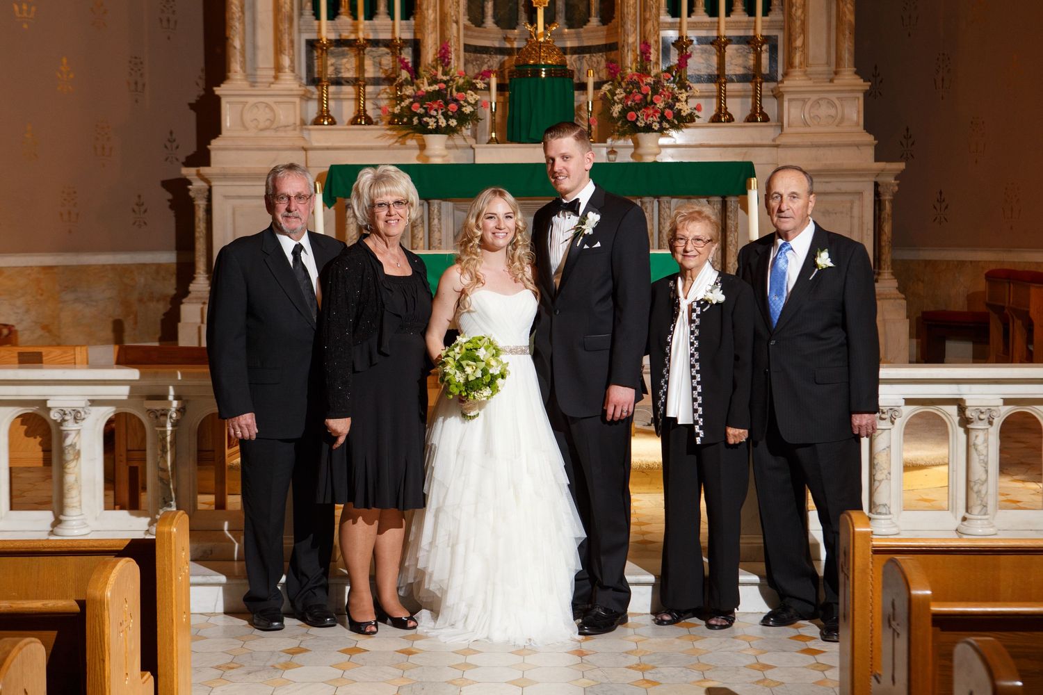 Group of people dressed formally posing together in a beautiful traditional church sanctuary with ornate altar.