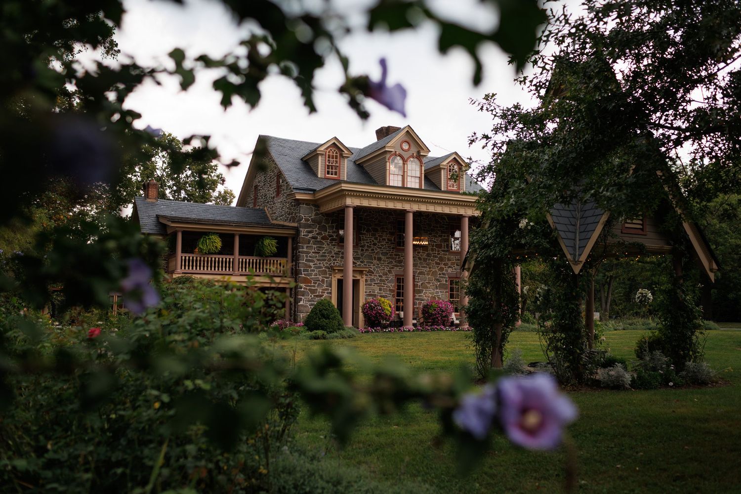A scenic view of a traditional colonial-style house nestled among lush green trees and landscaping.