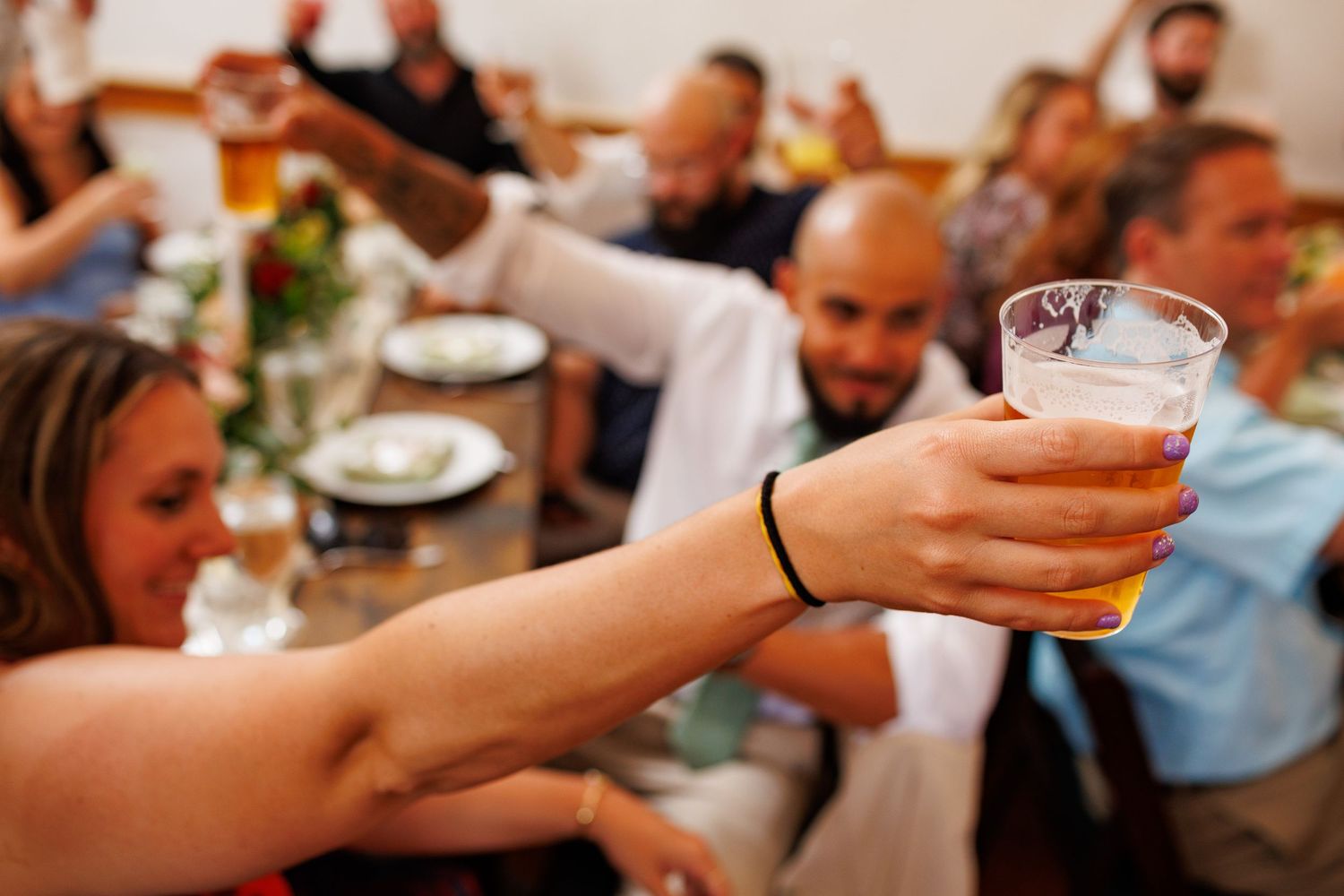 Wedding guests raising glasses in a joyful toast during colorful outdoor reception celebration.