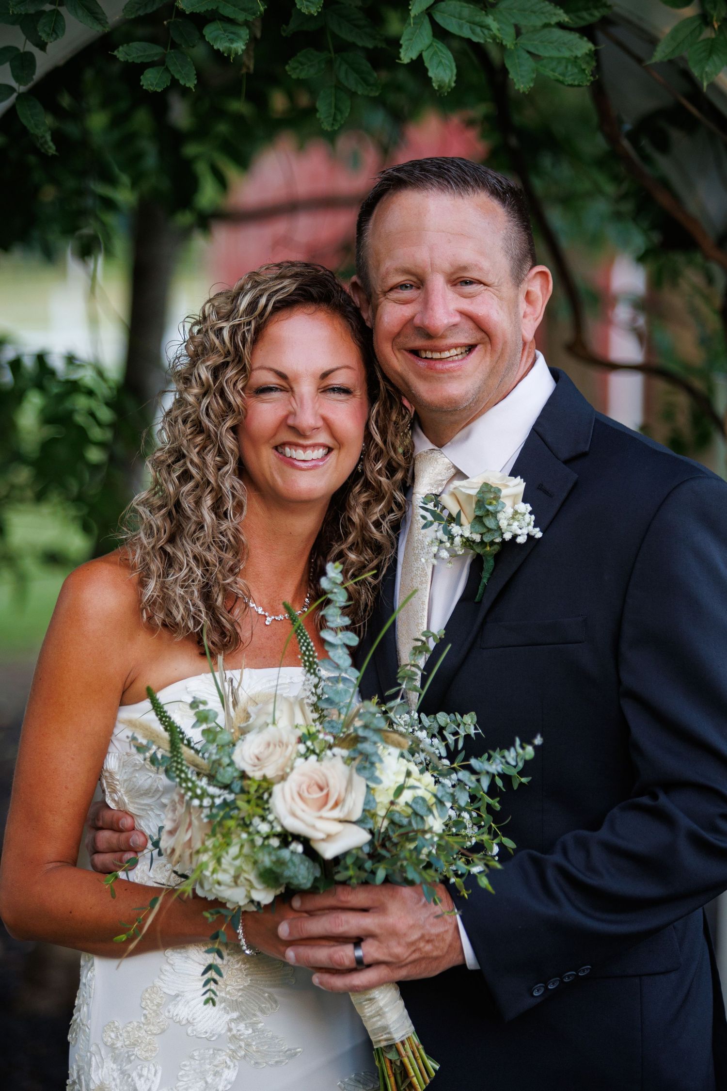 Happy wedding couple poses together holding a bouquet of white roses and eucalyptus greenery.