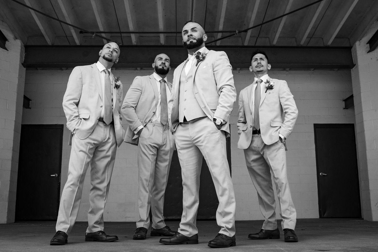 Black and white low-angle portrait of groom and three groomsmen in tan suits posing confidently.
