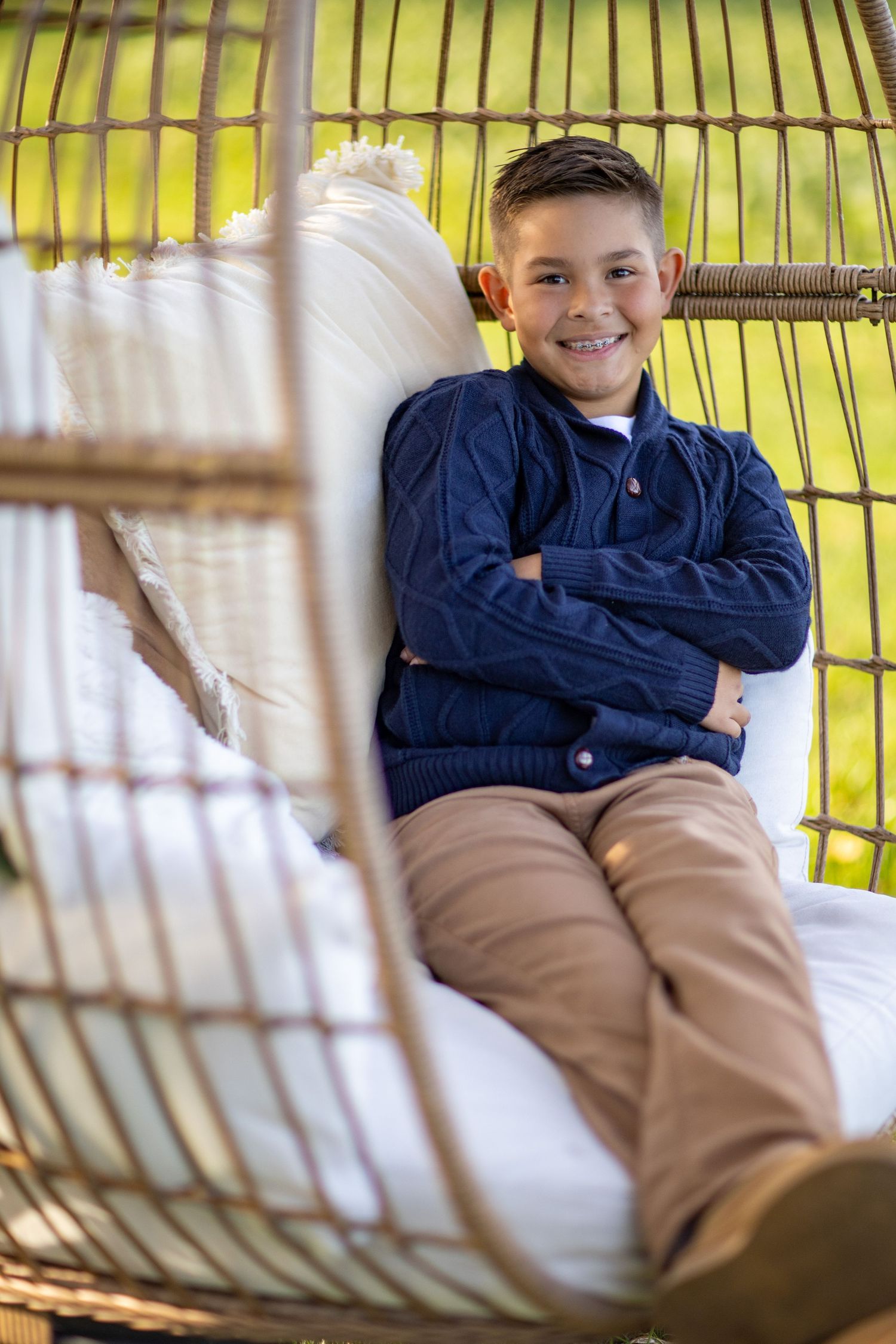 A child relaxes in a hanging rattan egg chair with white cushions against a yellow background.