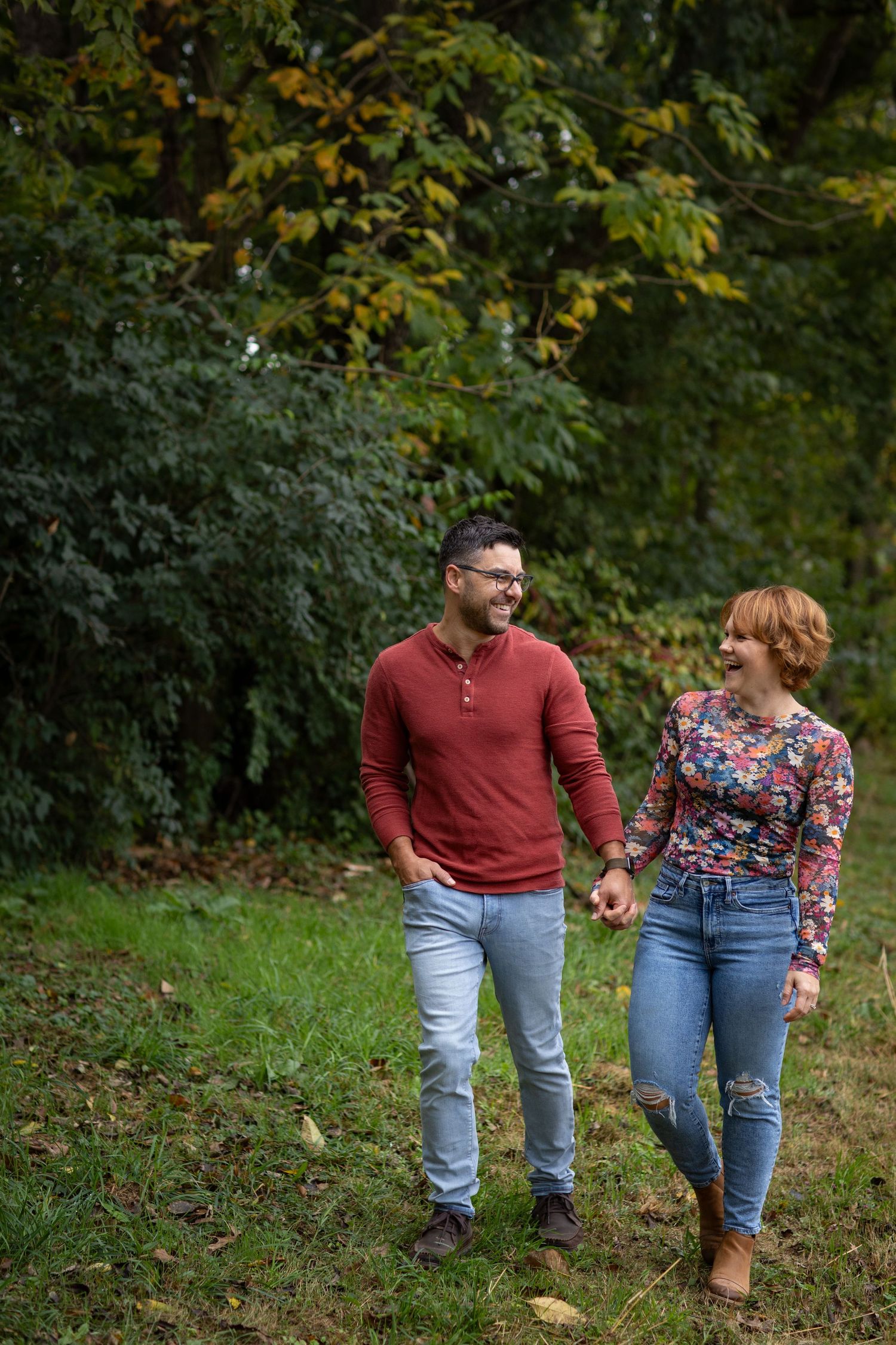 Couple walking together on a wooded path during autumn wearing casual denim and burgundy clothing.