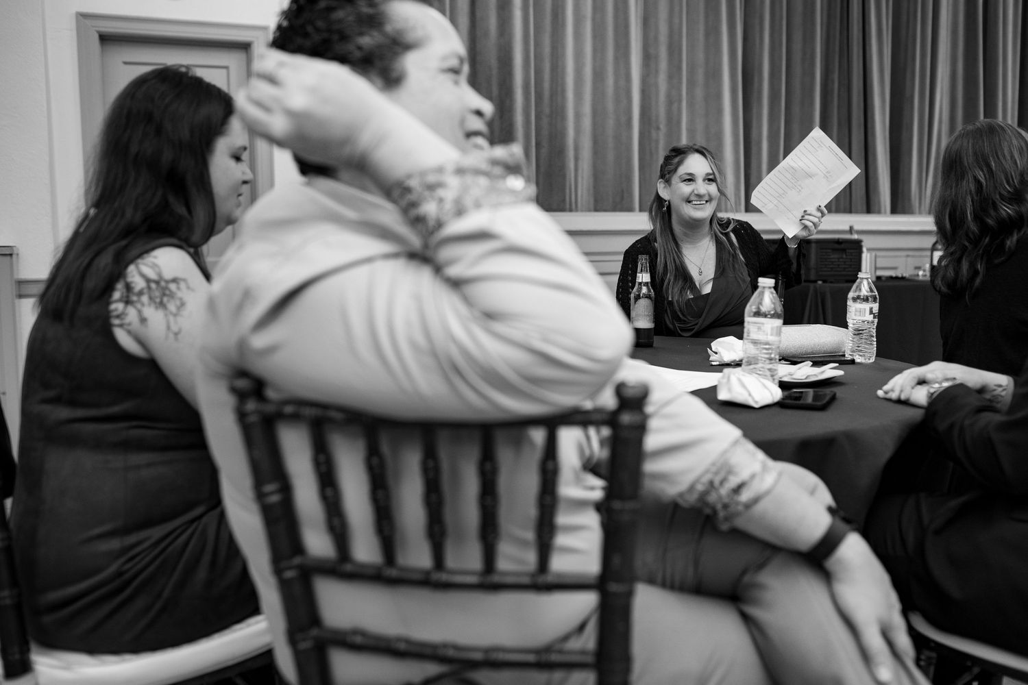 A candid black and white photo of people laughing together at a social gathering.