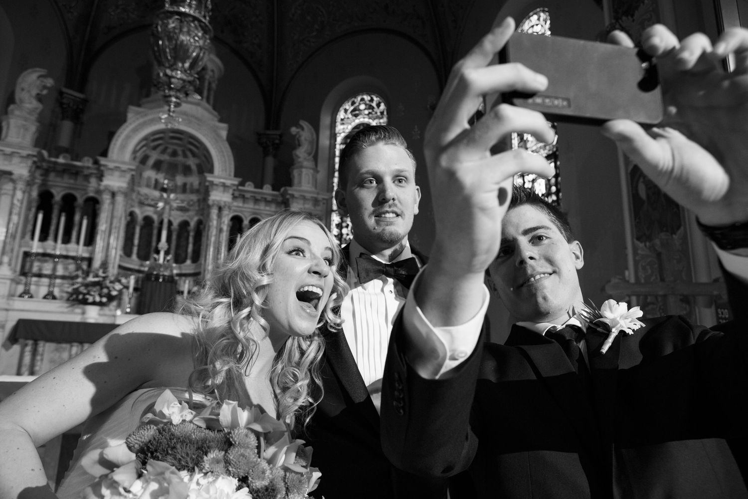 Wedding guests taking a joyful selfie together at an ornate venue during a formal celebration.
