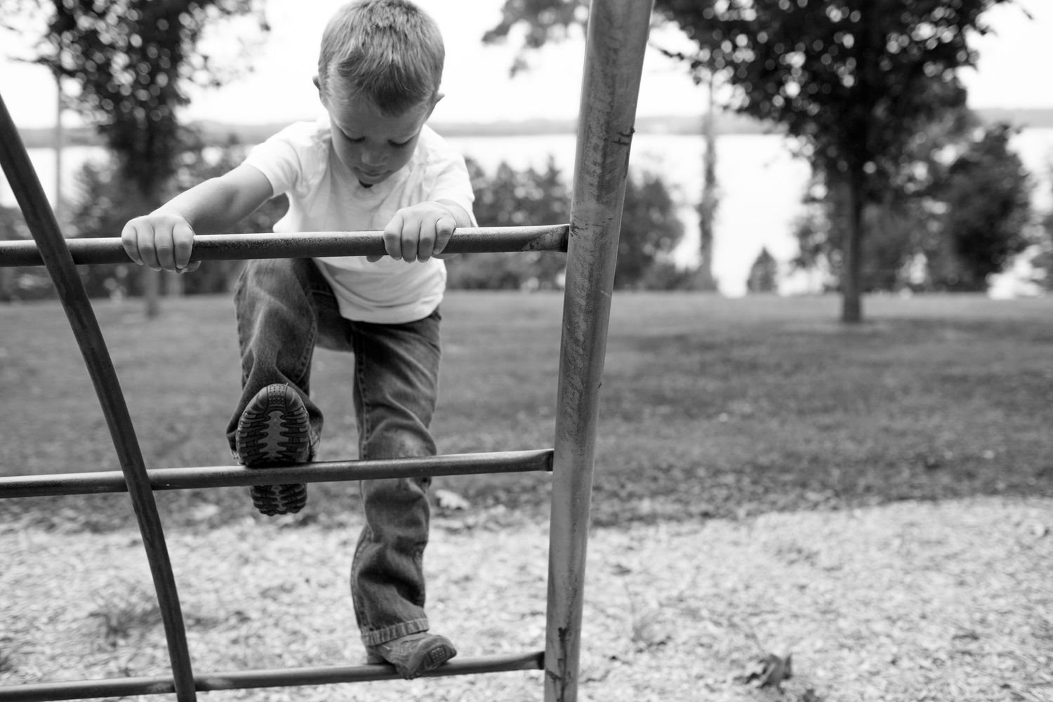 A young child climbs on playground equipment in a black and white photograph at a park.