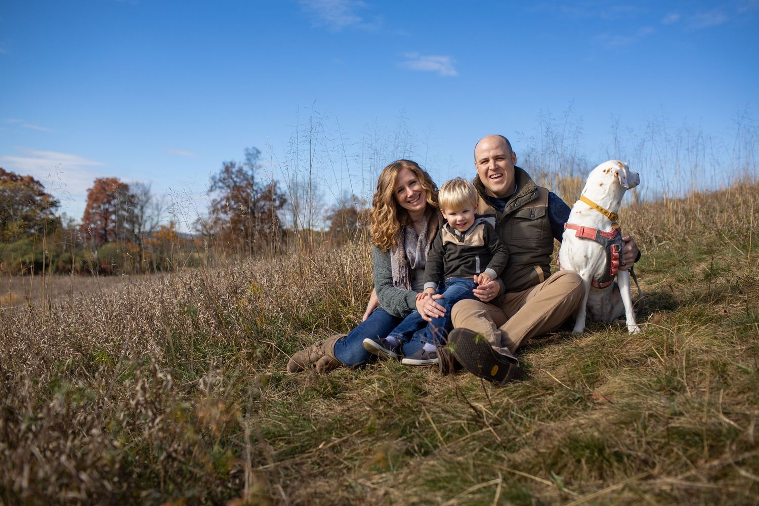 Family relaxing together on a scenic hillside with blue sky and autumn landscape in the background.