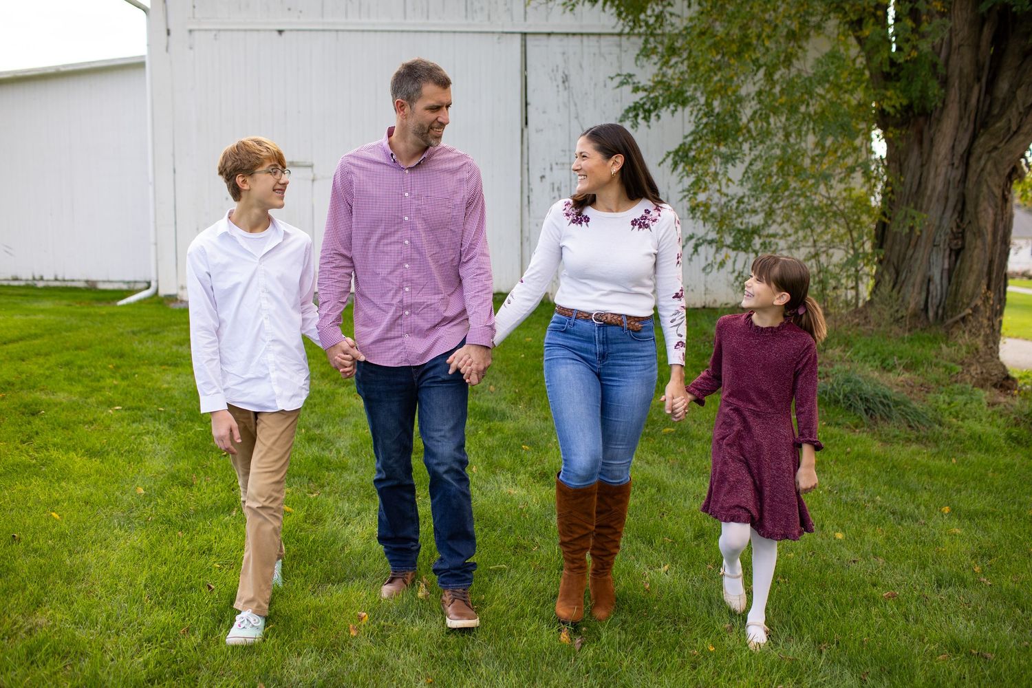 A family of four walking together on a green lawn, wearing coordinated fall sweaters and casual attire.