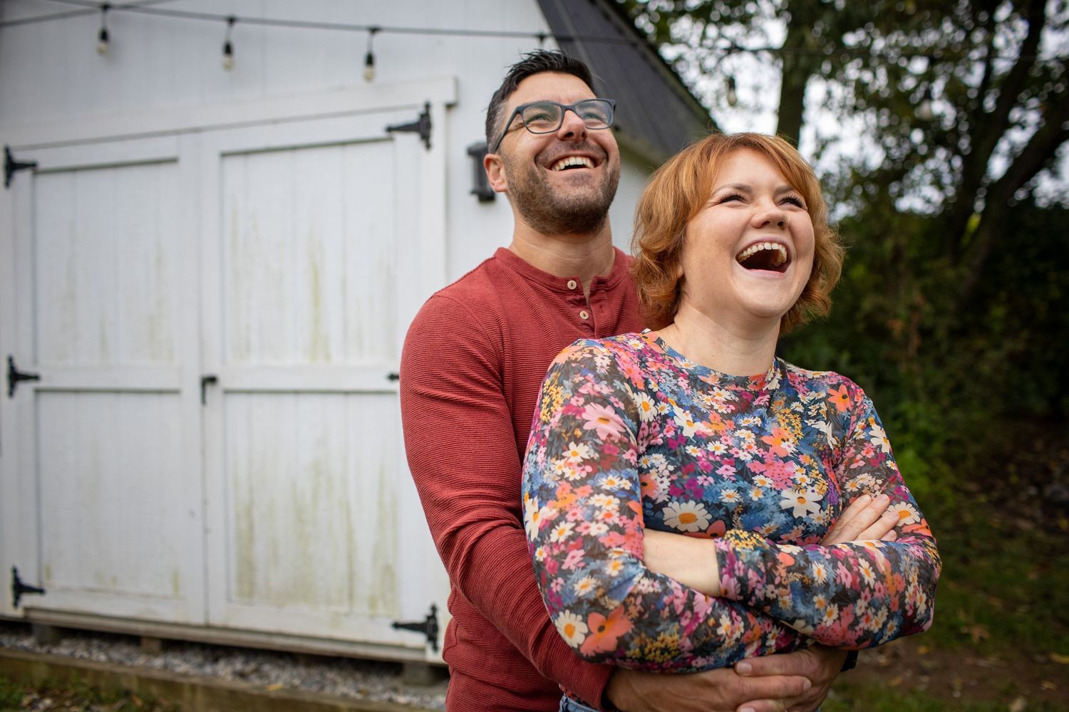 People share joyful laughter together against a white barn background.