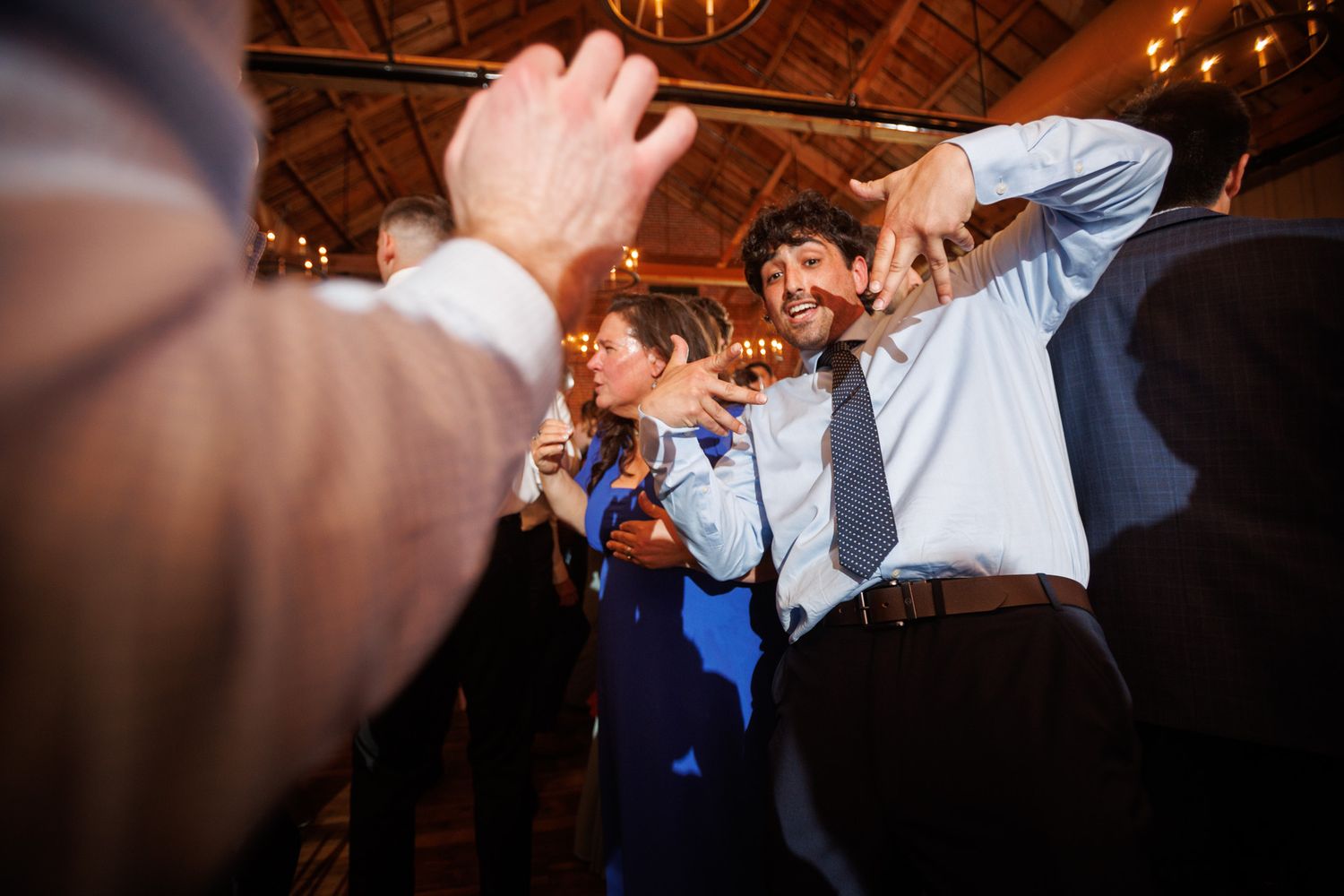 Guests dancing energetically at a wedding reception in a rustic venue with warm lighting.