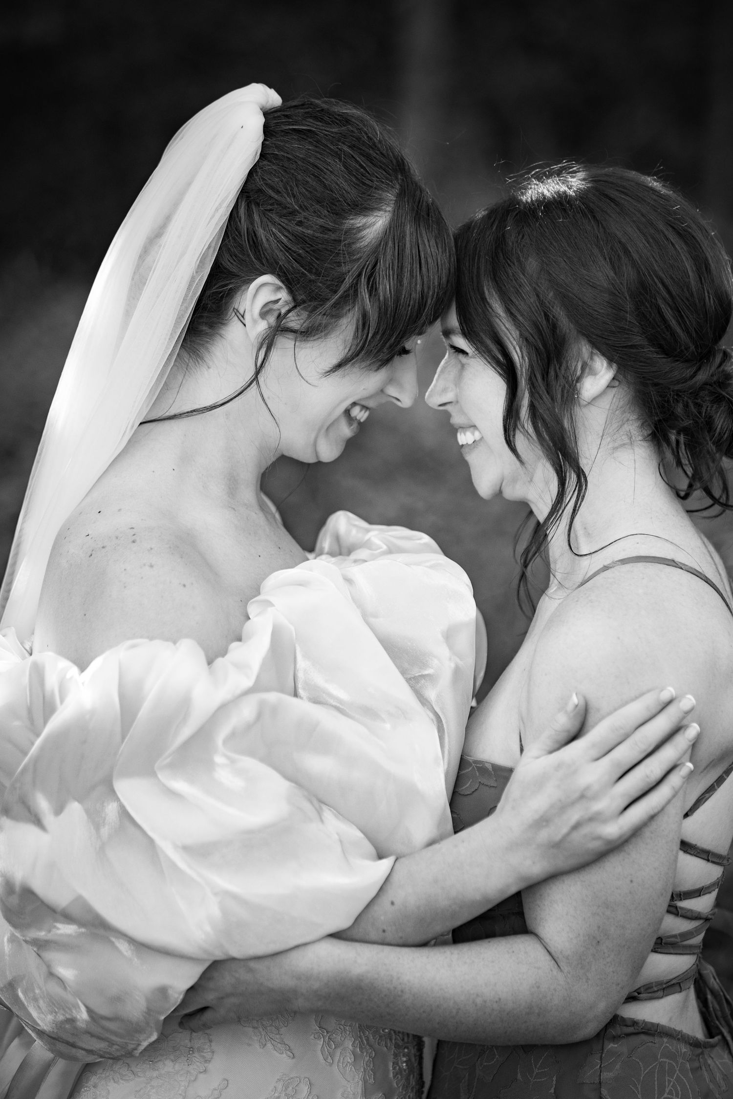 Two women in wedding attire share a joyful, intimate moment smiling face to face.