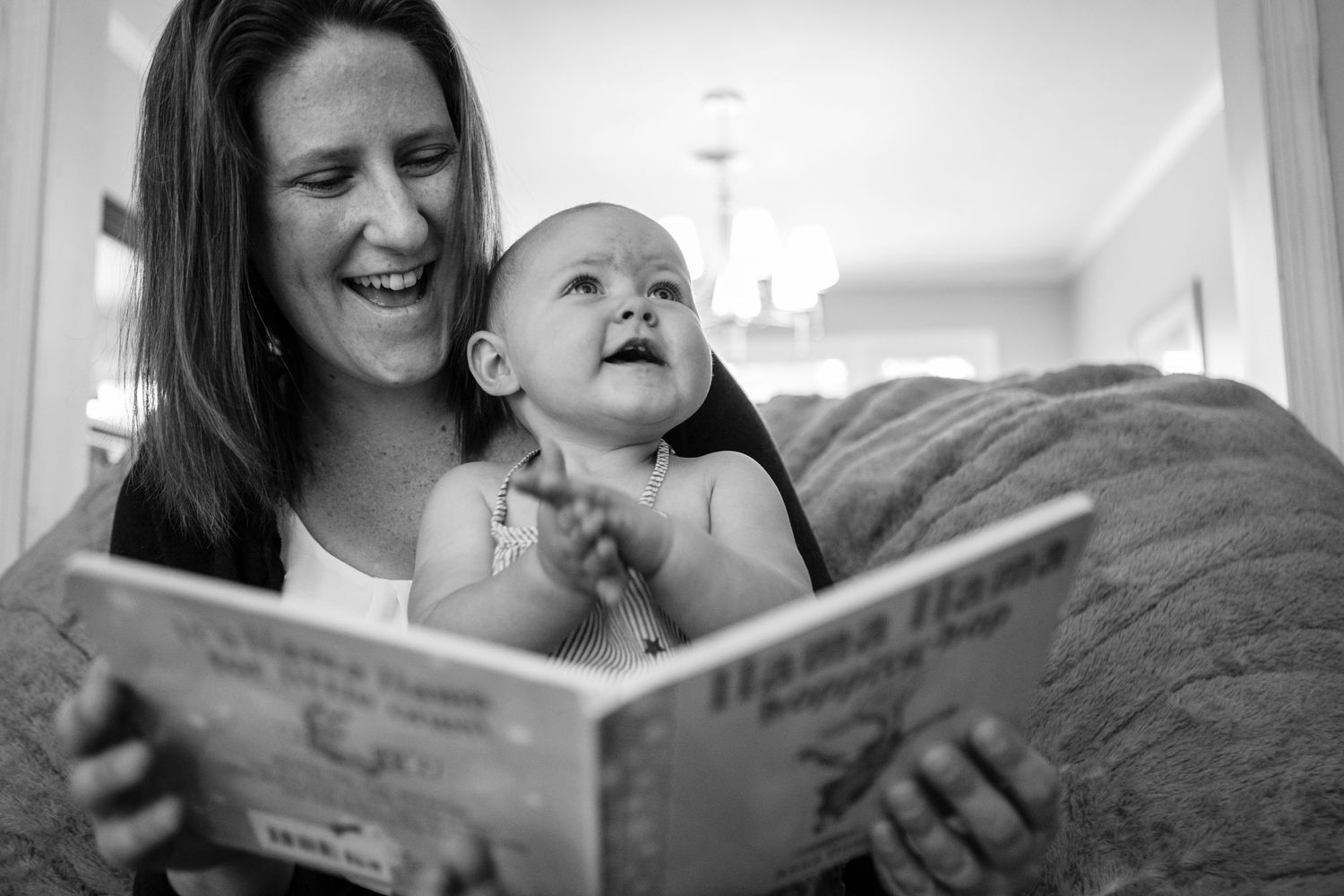 A joyful black and white moment of story time as an adult reads a book to a laughing baby.