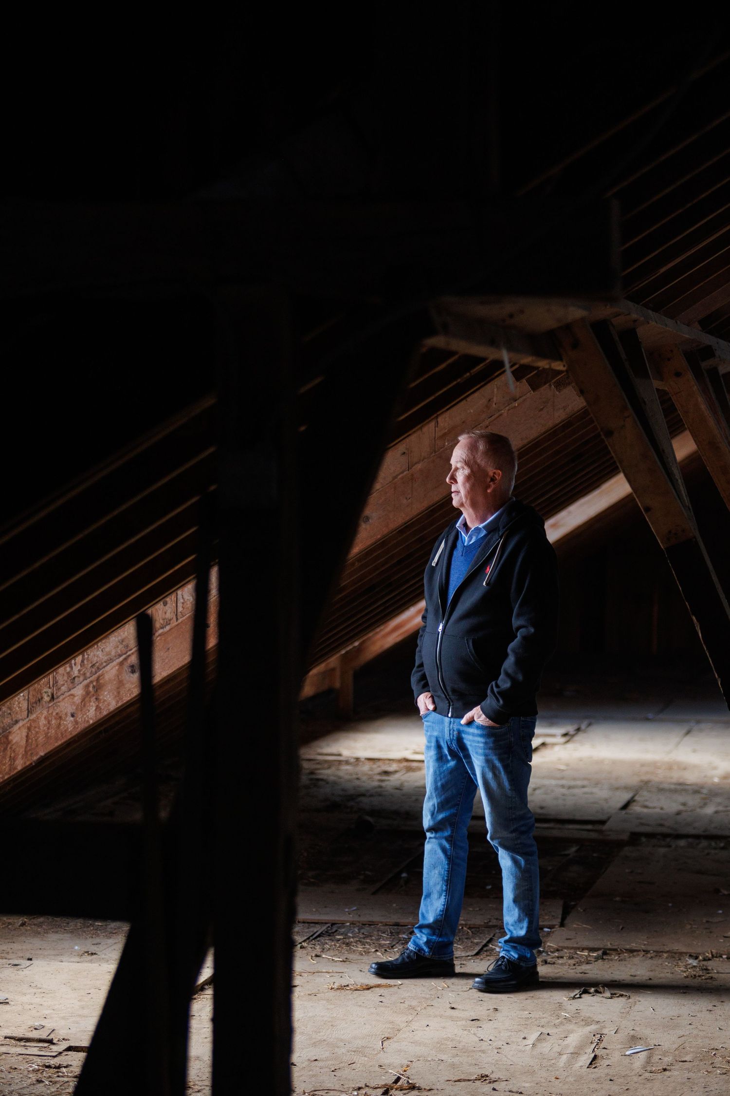 A person wearing blue stands in a dimly lit attic space with exposed wooden beams and rafters.