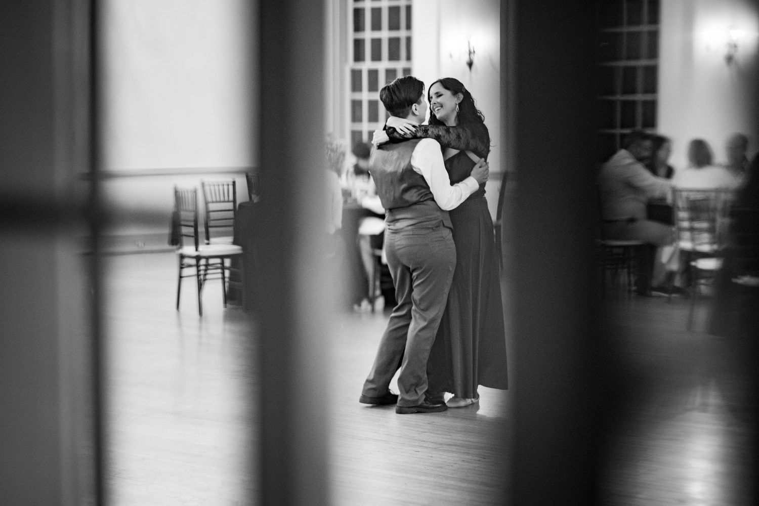 Couples dancing in dimly lit ballroom captured through artistic framing.