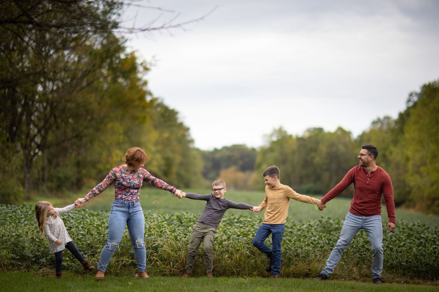 A playful line of people holding hands in a field during autumn.