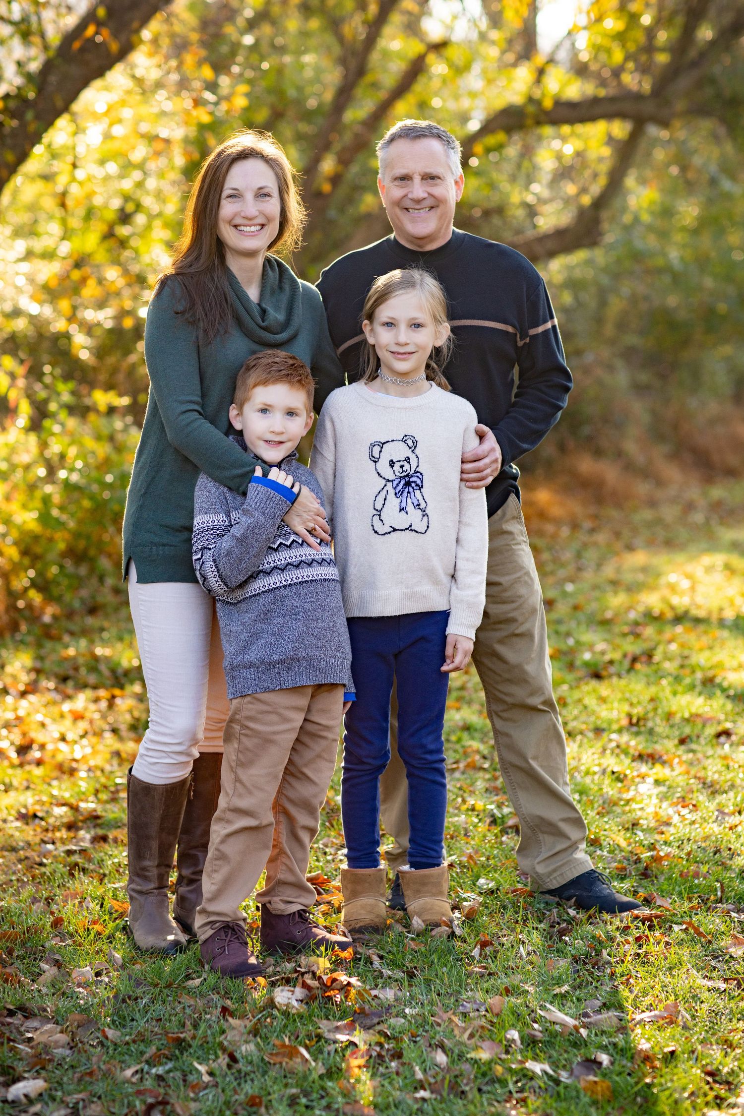 A family stands together in autumn foliage wearing coordinated casual outfits during an outdoor photo session.