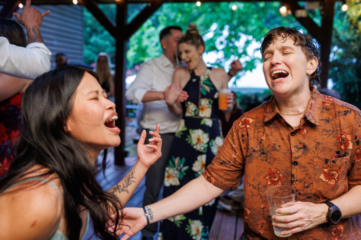Two wedding guests laugh together at lively outdoor wedding reception celebration.