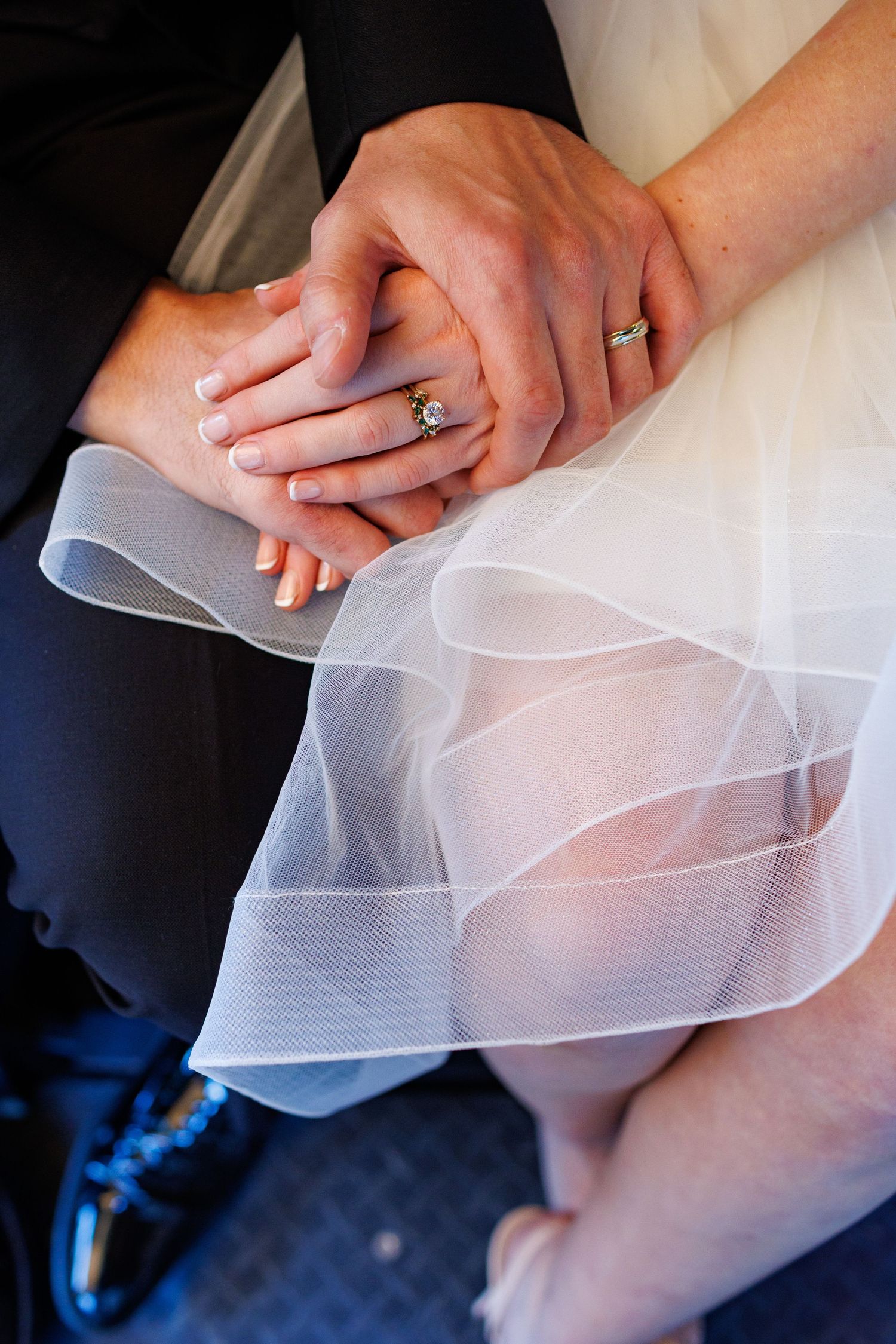 Close-up of bride and groom holding hands showing diamond engagement ring and wedding bands.