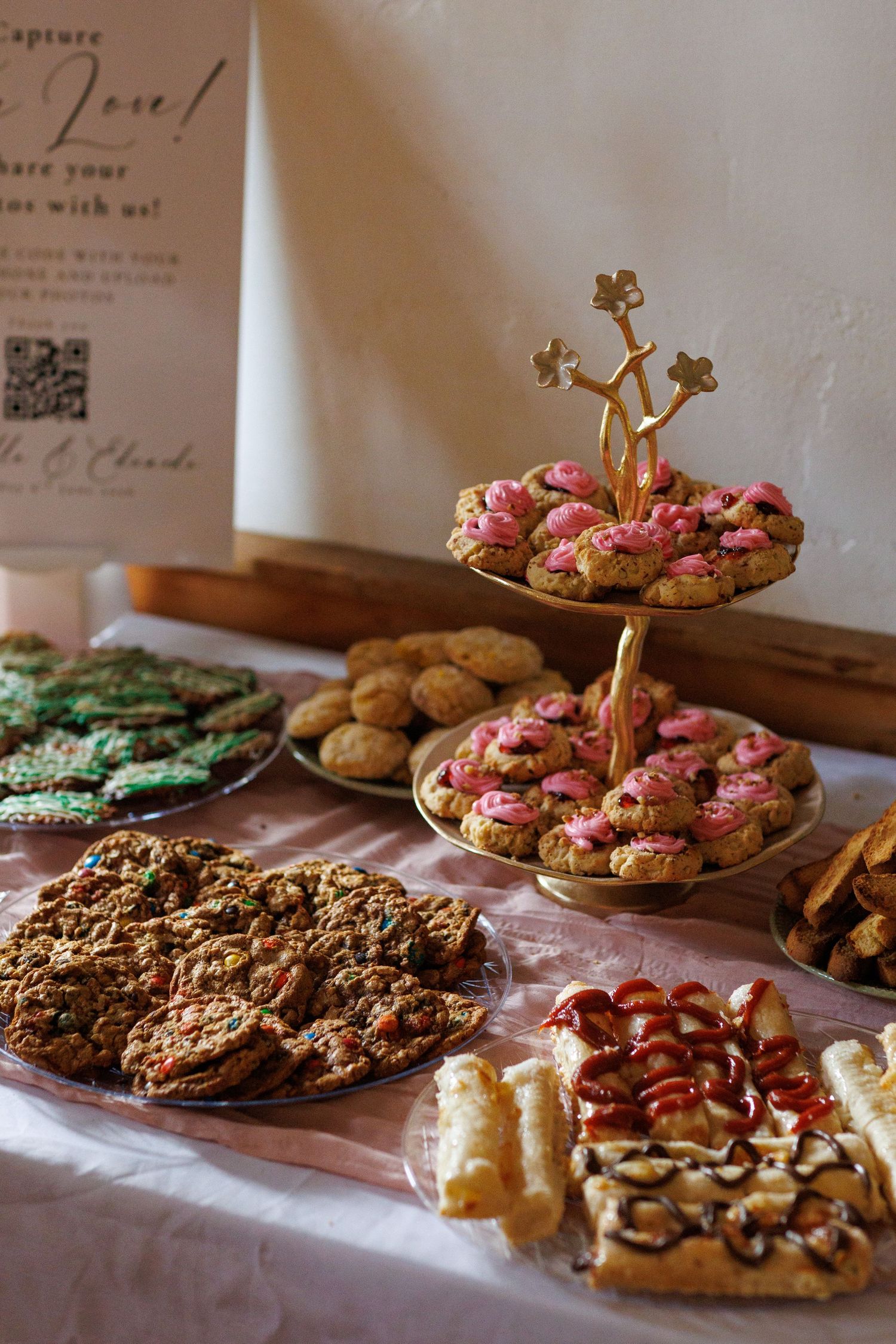 Assorted wedding dessert table with pink frosted cookies, green treats, granola bars, and pastries on display.