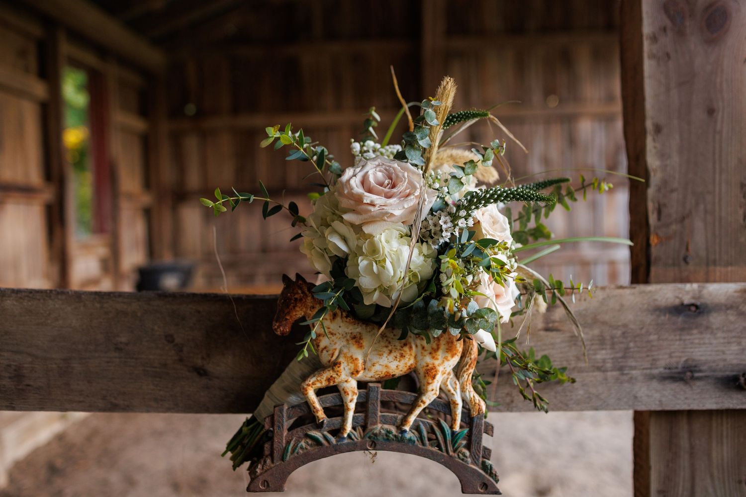 Rustic wedding floral arrangement with white roses and greenery displayed on a decorative deer figurine inside a wooden barn.
