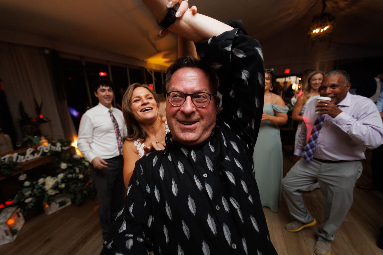 A group dances and celebrates together at what appears to be a lively wedding reception or party.