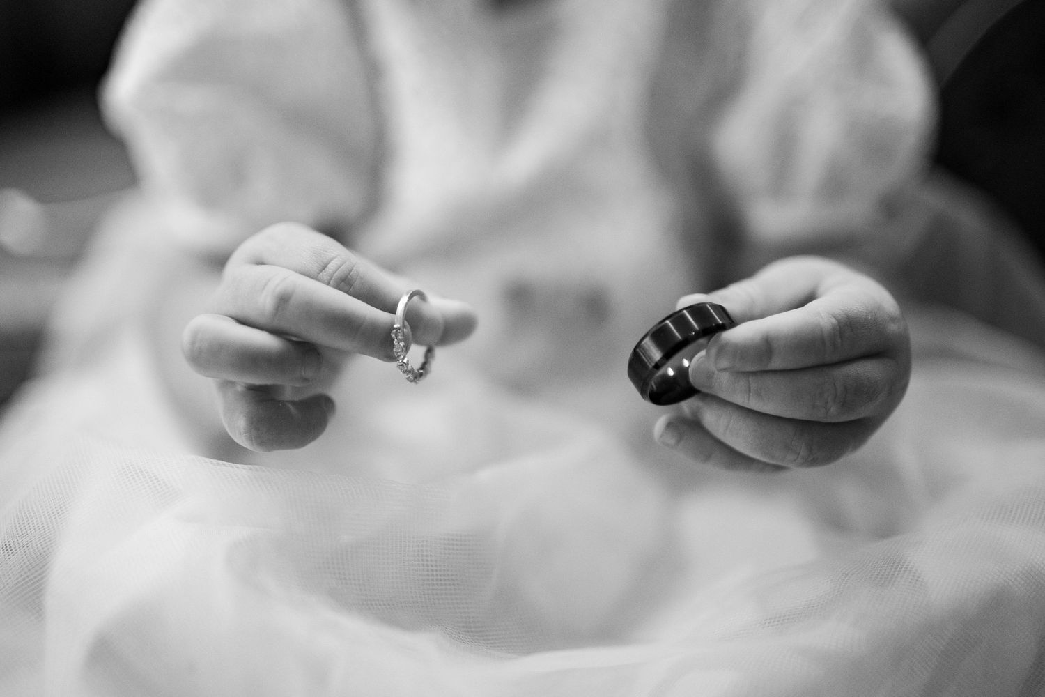 Grayscale close-up captures hands holding a delicate engagement ring in a romantic moment.