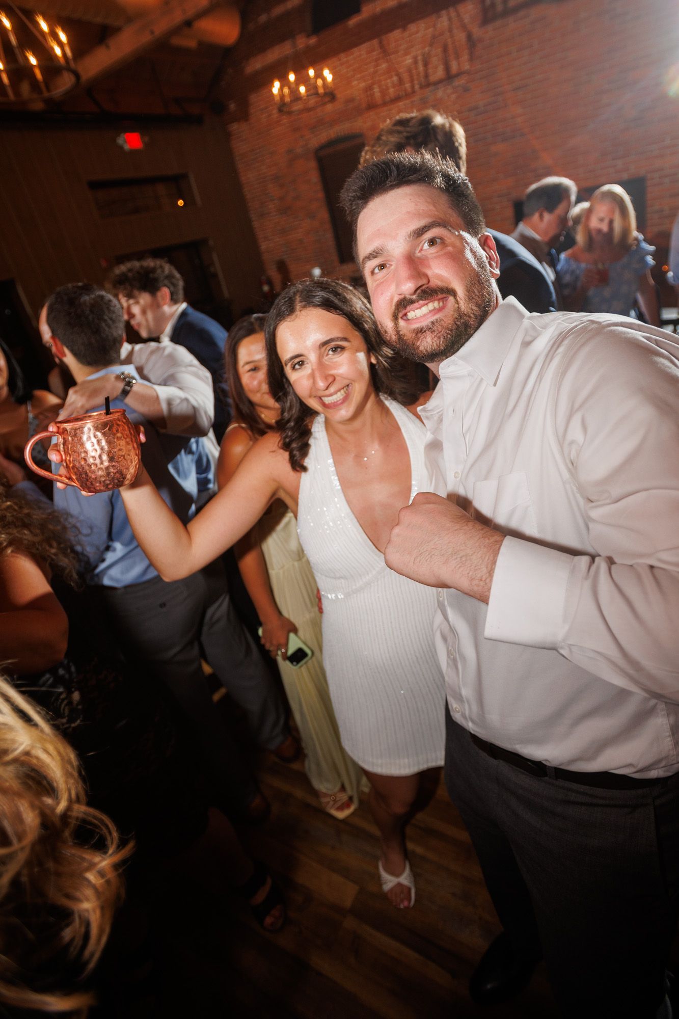 Couple smiling and posing together on a wedding reception dance floor in a rustic brick venue.